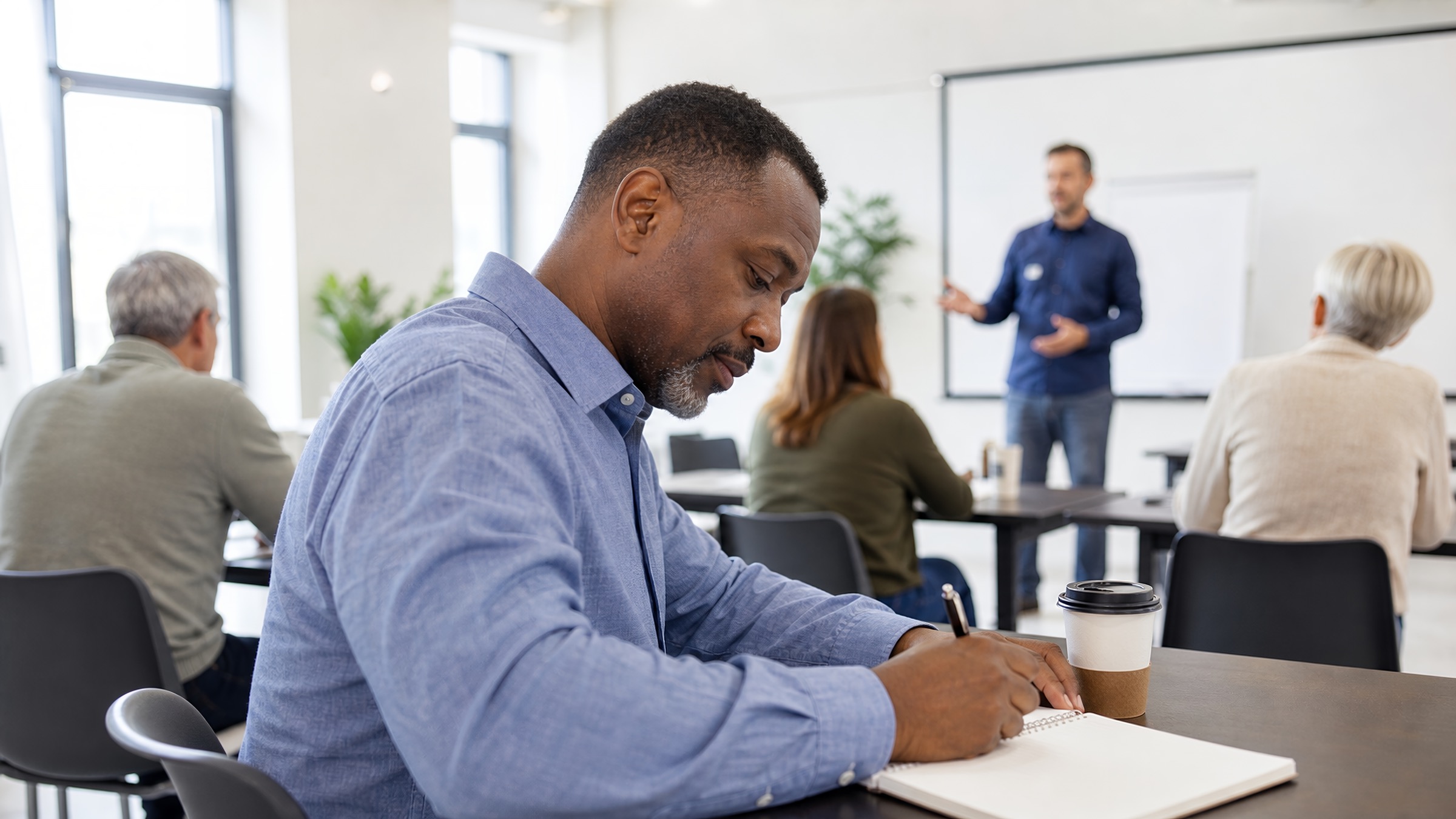 Man writing in a notebook during a small classroom training session.