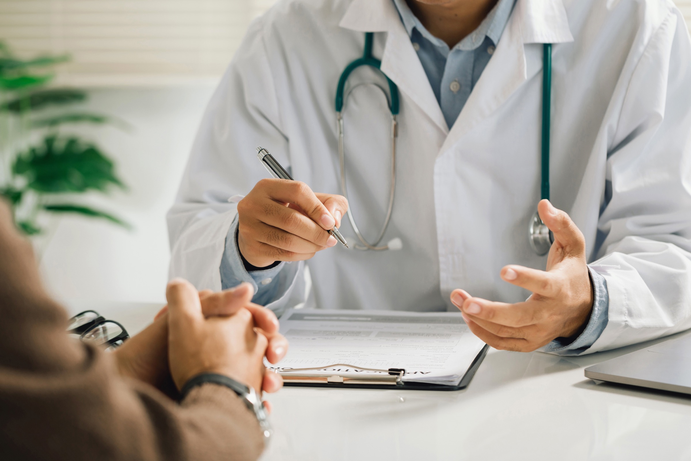 Healthcare professional in a white coat discussing a document with a person across a desk.